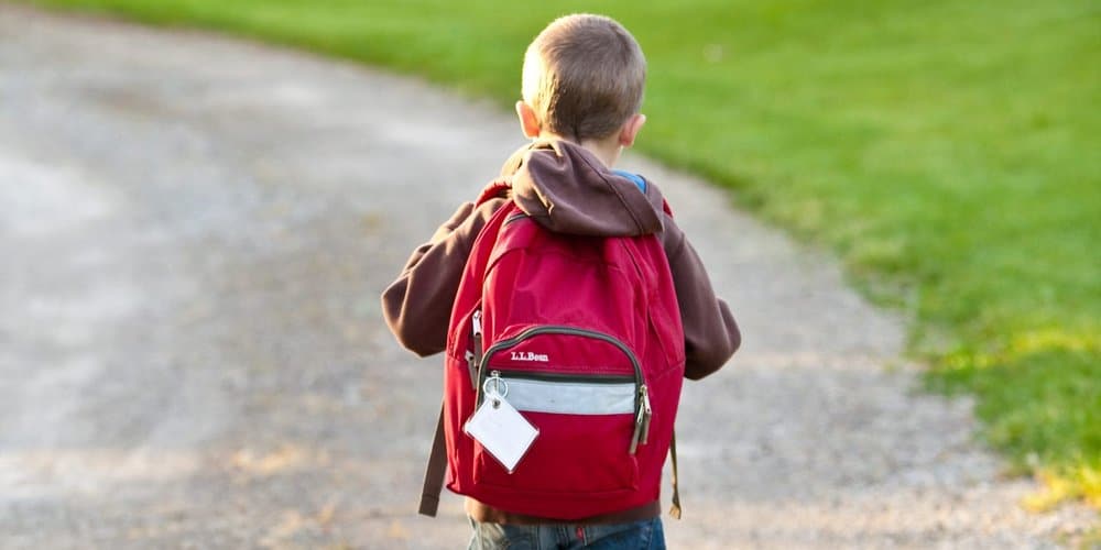 boy in brown hoodie carrying red backpack