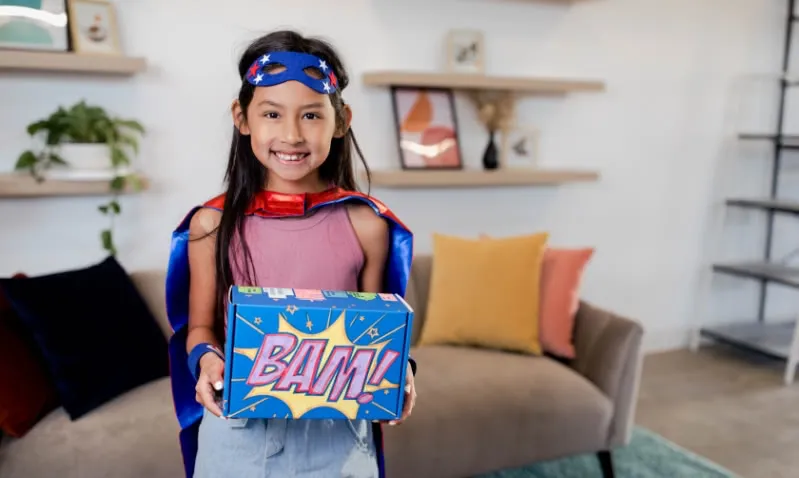 girl dressed as superhero holding superhero box