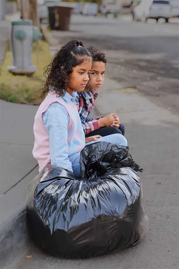 siblings with trash bags sitting on sidewalk