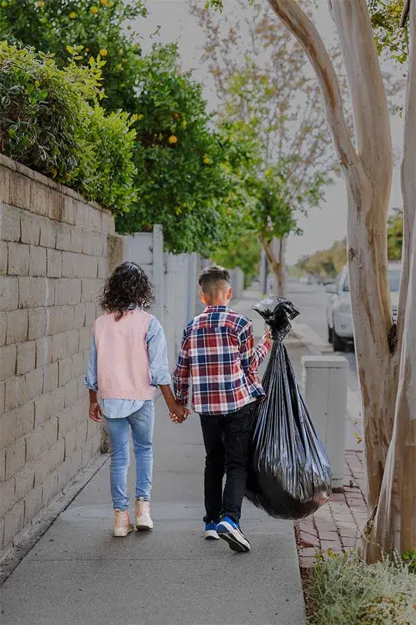 siblings-with-trashbags-walking-down-sidewalk