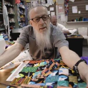 man sitting at a table looking over fabric scraps