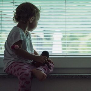 lone child looking out window blinds