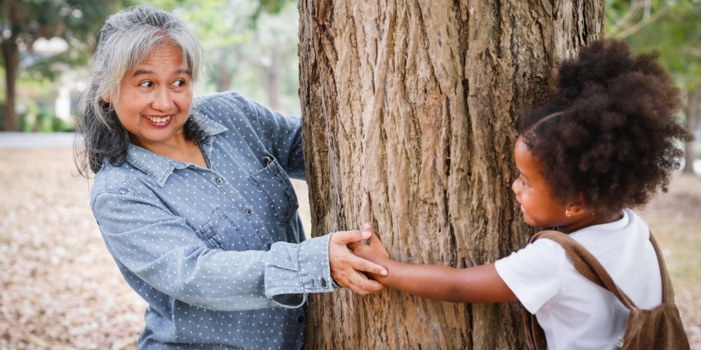 Woman playing behind tree with her niece is someone who qualifies for kinship care