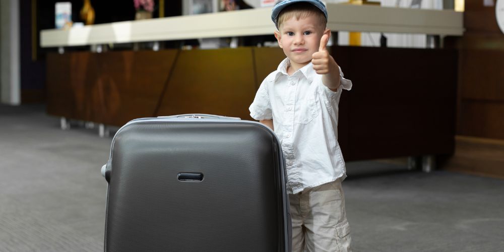 Boy holding a suitcase giving a thumb up