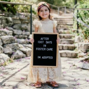 A girl holding a sign declaring she is adopted from foster care