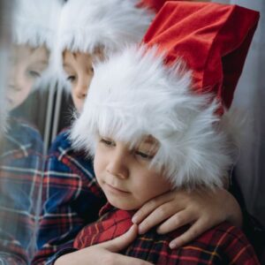 two boys wearing santa hats looking out the window