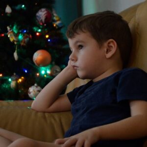 A sad little boy sitting in a chair by a Christmas tree
