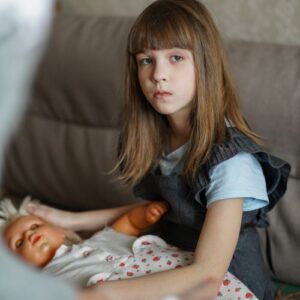 A little girl with a doll looking seriously into the camera