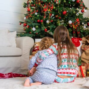 Two girls sitting facing a Christmas tree with their backs to the camera