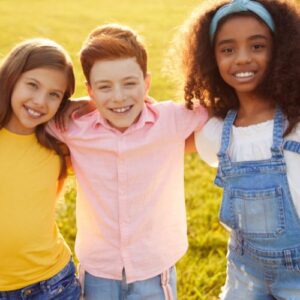 Three smiling kids in the sun outside