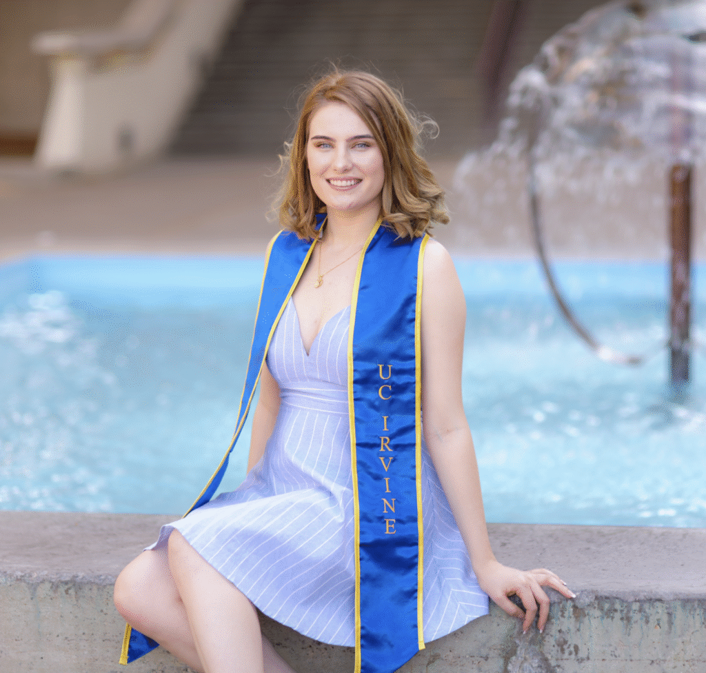 Family Fellow sitting on the edge of a fountain wearing her graduation sash
