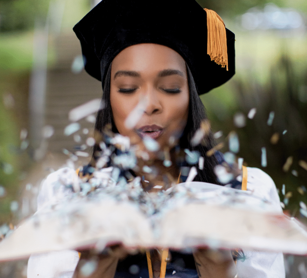 Foster Love Family Fellowship scholar in cap and gown blowing confetti out of an open book