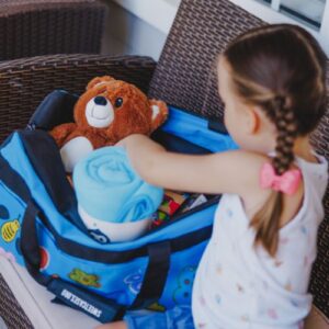A little girl opening a duffle bag Sweet Case with a teddy bear and blanket