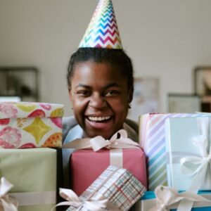 girl in a birthday hat surrounded by piles of gifts
