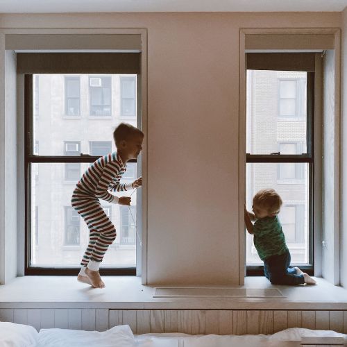 kids jumping on bed by windows in city