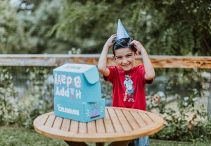 boy putting on birthday hat at a table with an open Birthday Box