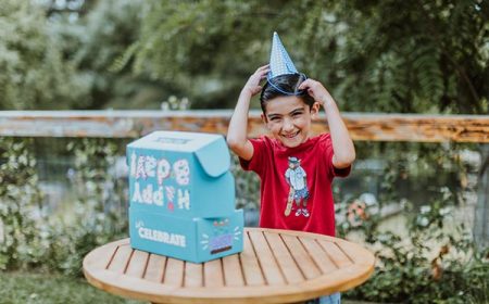 boy putting on birthday hat at a table with an open Birthday Box
